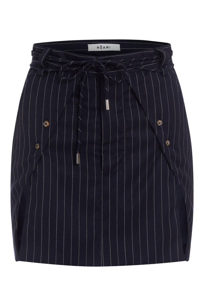 Navy Pinstripe Pre-Order | RONNIE SKIRT *SHIPS END OF NOVEMBER. Please note that any order containing a pre-order item/s will be shipped when pre-order item/s become available. We suggest placing two orders if you'd like to receive now available items quicker. Paneled skirt featuring a self-fabric waist tie tunneled through two rows of belt loops. Double front vents are secured by horn buttons. Slightly lengthened back for added coverage. 