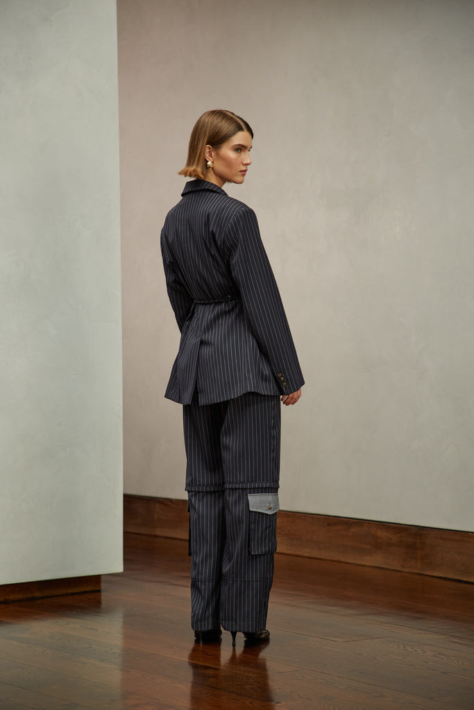 Navy Pinstripe Ronnie Blazer Oversized 90's inspired blazer featuring a fixed self-fabric waist tie, cargo pocket detail on left sleeve, two standard flap pockets at hips, and custom selected horn buttons. Ana is 5'9