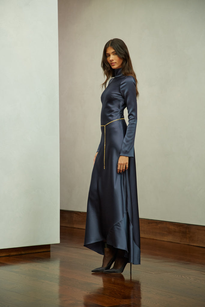 Navy Florence Dress This long sleeved satin gown is coveted for its fluid, liquid-like drape and movement. It is distinguished by a cowl turtleneck silhouette and plunging open back cutout. Includes gold chain belt.Styling tip: Option to wear belt wrapped as a bracelet, or as a lariat cascading down the open back.