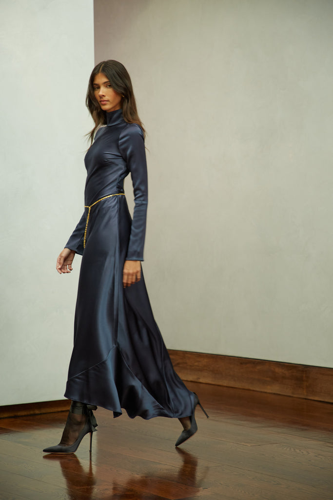 Navy Florence Dress This long sleeved satin gown is coveted for its fluid, liquid-like drape and movement. It is distinguished by a cowl turtleneck silhouette and plunging open back cutout. Includes gold chain belt.Styling tip: Option to wear belt wrapped as a bracelet, or as a lariat cascading down the open back.