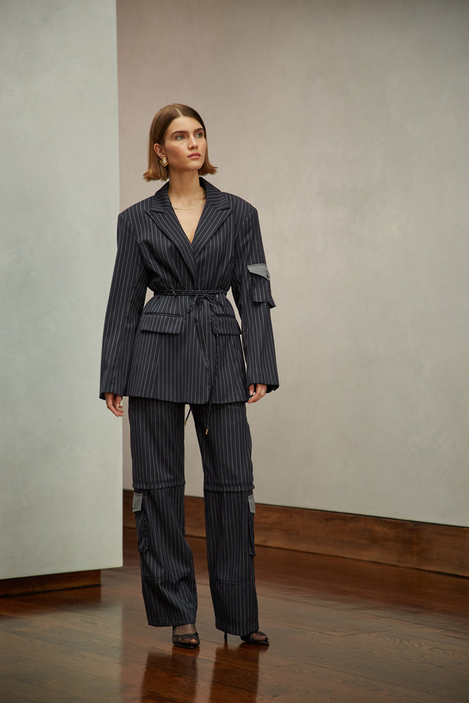 Navy Pinstripe Ronnie Blazer Oversized 90's inspired blazer featuring a fixed self-fabric waist tie, cargo pocket detail on left sleeve, two standard flap pockets at hips, and custom selected horn buttons.Style with The Ronnie Trouser | The Ronnie Corset | The Ronnie Skirt