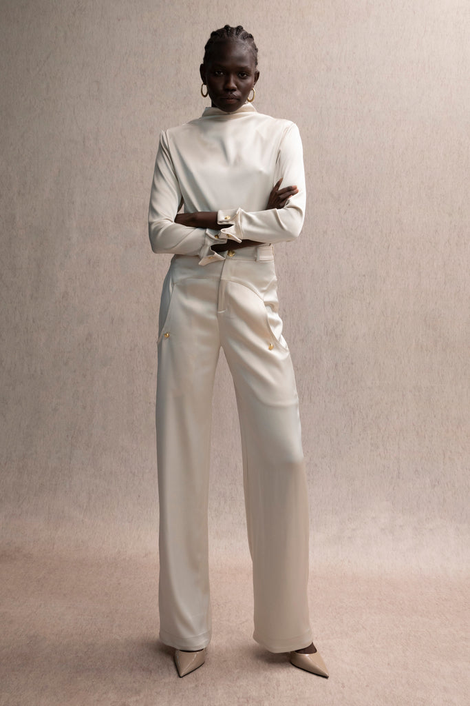 Champagne Vivien LS Top Elevate your wardrobe with this silky-soft and versatile satin top.-Cowl neckline with stacked collar-Self-loops with gold knot buttons at back neck-Removable shoulder pads with interior pockets-Hidden zip at back-Turnback cuff with gold knot button-Fluid drape with tailored structure-Finished with French seamsWe recommend ordering your usual size.Styled with the Vivien Pant & Ava Skirt