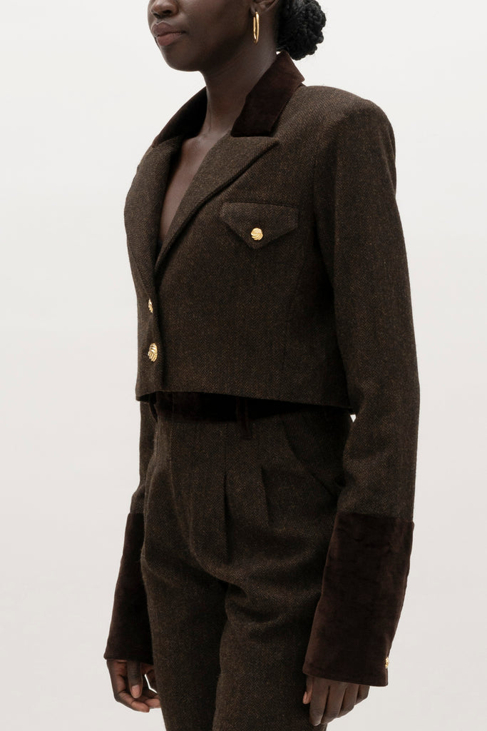 Brown Herringbone Camilo Jacket The Camilo Jacket: A fusion of classic tailoring and refined detailing, this cropped jacket elevates timeless tweed with modern touches.-Cropped herringbone blazer -Soft Merino wool-Contrast velvet combo fabric at the collar and lapel-Flap pocket with single gold knot button closure-Structured padded shoulder -Gold knot buttons at center front-Gold knot button on exterior cuff-Fully lined Crafted with Merino wool certified by the Wool Integrity Programme, ensuring farms adhere to the Five Freedoms of animal welfare. We recommend ordering your usual size.Styled with the Raymond Trouser, Zoey Tank, & Kate Short