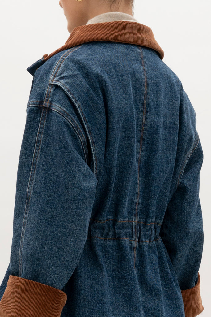 Medium Indigo Torrey Jacket A corduroy collar and gold buttons elevate this classic silhouette, while a drawcord waist lets you personalize the fit. Perfect for layering. -Premium Japanese denim-Cinched-waist jacket-Corduroy-faced collar-Funnel neck-Drawcord tunnel at waist-Welt pockets at front-Self-fabric placket with gold knot buttons-Corduroy faced cuff for option to roll-Flannel lined interior♻️ Environmentally conscious: Made with up-cycled Japanese denim that is produced with reduced CO2 emissions and water-conserving processes. We recommend ordering your usual size.Styled with the Torrey Jean & Olivia Turtleneck  