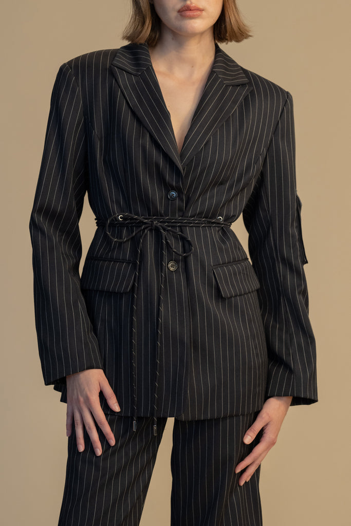 Navy Pinstripe Pre-Order | RONNIE BLAZER *SHIPS END OF NOVEMBER. Please note that any order containing a pre-order item/s will be shipped when pre-order item/s become available. We suggest placing two orders if you'd like to receive now available items quicker. Oversized 90's inspired blazer featuring a fixed self-fabric waist tie, cargo pocket detail on left sleeve, two standard flap pockets at hips, and custom selected horn buttons.