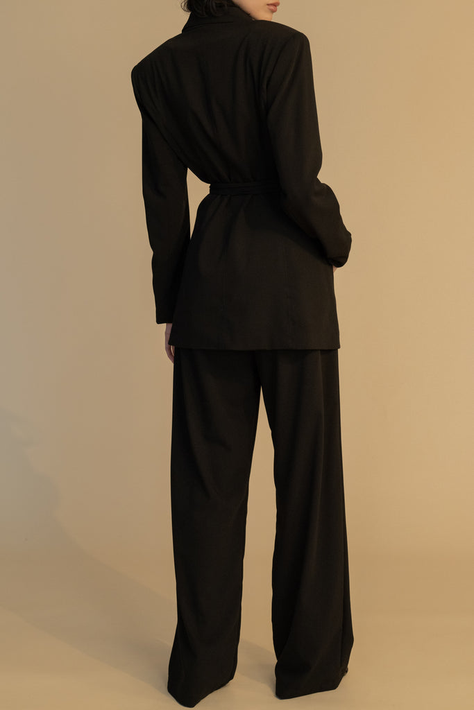Black RHODES BLAZER This mid-length blazer features a detachable waist tie, allowing you to create a range of looks. The tailored single- breasted style features shoulder pads and front welt pockets. The Kat Trouser compliments the blazer perfectly.