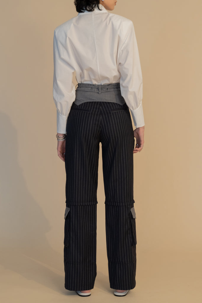 Navy Pinstripe Pre-Order | RONNIE TROUSER *SHIPS END OF NOVEMBER. Please note that any order containing a pre-order item/s will be shipped when pre-order item/s become available. We suggest placing two orders if you'd like to receive now available items quicker. High-rise lightweight tailored trouser featuring contrasting waistband with self-fabric tie tunneled through two rows of belt loops. Featuring a relaxed leg fit with cargo style pockets and horn buttons.