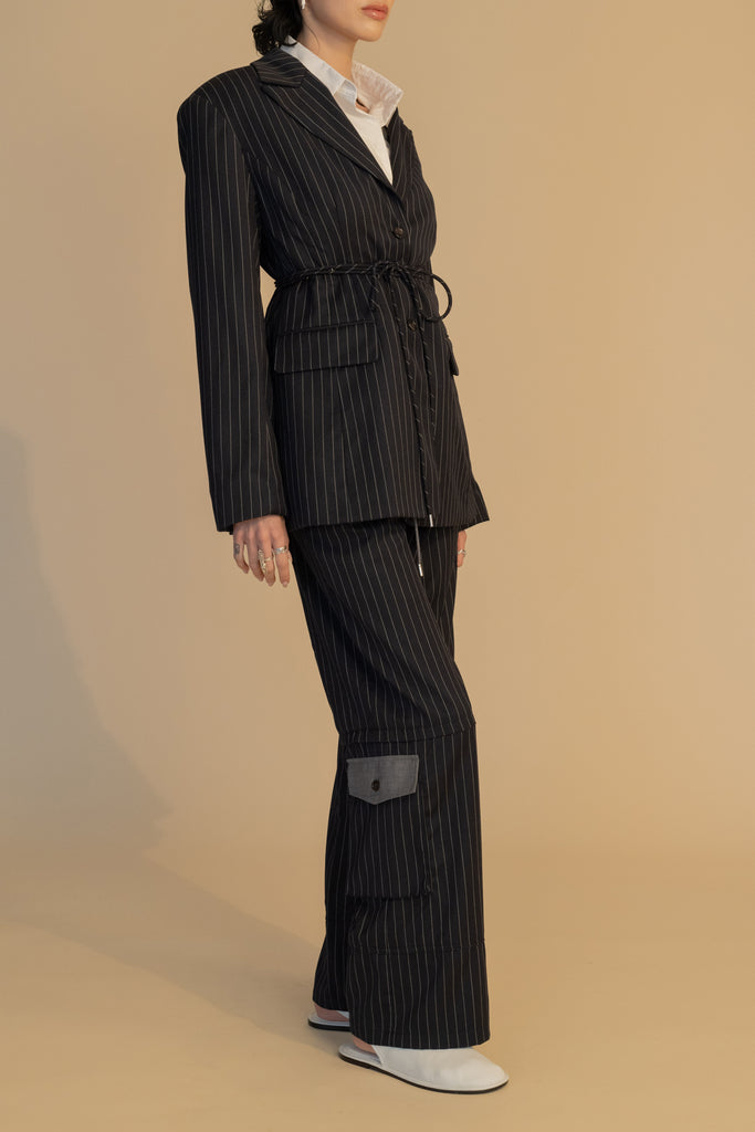 Navy Pinstripe Pre-Order | RONNIE TROUSER *SHIPS END OF NOVEMBER. Please note that any order containing a pre-order item/s will be shipped when pre-order item/s become available. We suggest placing two orders if you'd like to receive now available items quicker. High-rise lightweight tailored trouser featuring contrasting waistband with self-fabric tie tunneled through two rows of belt loops. Featuring a relaxed leg fit with cargo style pockets and horn buttons.