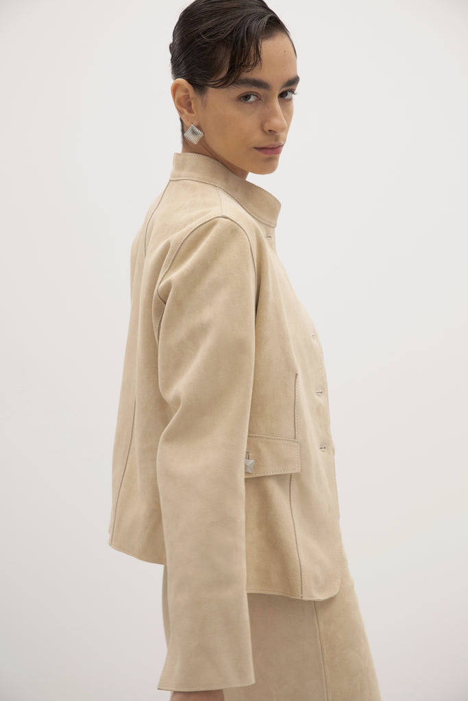 Sand Hyde Jacket -Structured vintage inspired jacket with mandarin collar-Princess seams contour the bodice and waist -100% calf leather (suede) -Ornate front button hardware with interior stay buttons for durability-Hidden zipper pockets integrated into front princess seams-Buttoned pocket flaps for visual detail (non-functional flap; real pocket hidden beneath)-Clean-finished hem, sleeve, and collar with subtle edge stitch detailing-Hidden interior chest pocket with zipper closure-Vents at back of sleeves-Fully lined Ingryd is 5'10
