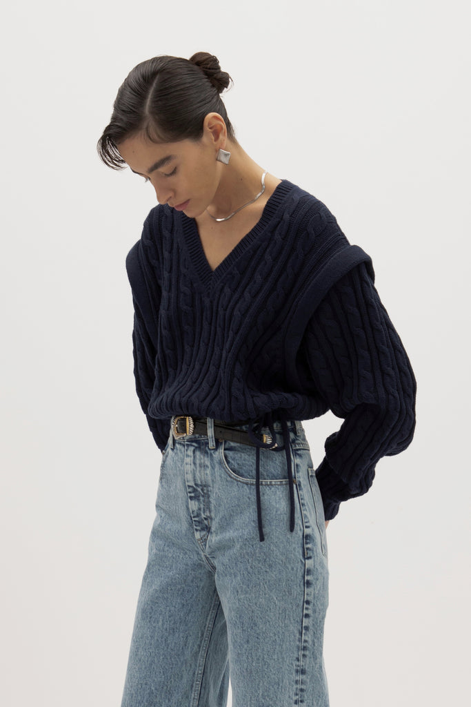 Navy Isabel Sweater Made with 100% cotton yarn, this convertible cable knit sweater features hidden snaps for the option to remove the sleeves. Knit draw cord at waist for choice to cinch or neatly tuck into your favorite jeans. A quintessential seasonless piece.*The top left and right of the removable sleeves will have either a red or white small sewn on marker, indicating which sleeve goes where for ease when placing back on. Ingryd is 5'10