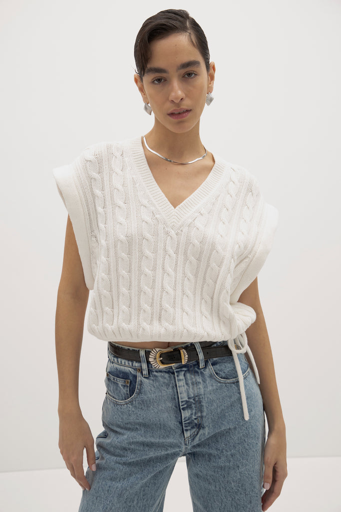 White Isabel Sweater Made with 100% cotton yarn, this convertible cable knit sweater features hidden snaps for the option to remove the sleeves. Knit draw cord at waist for choice to cinch or neatly tuck into your favorite jeans. A quintessential seasonless piece.*The top left and right of the removable sleeves will have either a red or white small sewn on marker, indicating which sleeve goes where for ease when placing back on. Ingryd is 5'10