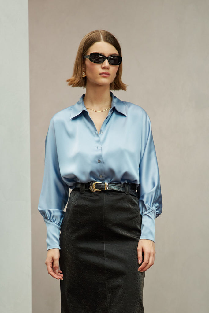 Sky Marna Shirt A silky button down featuring blouson sleeves. Composed of wrinkle resistant vegan silk, this top includes mother of pearl buttons, concealed zippers at wrists, and removable shoulder pads. 