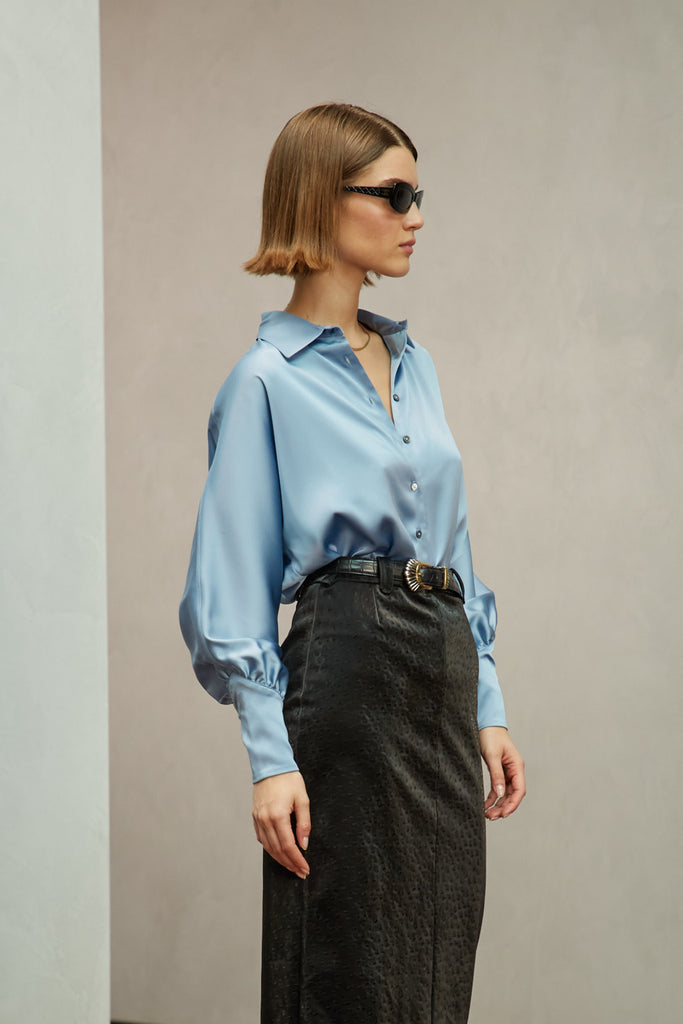 Sky Marna Shirt A silky button down featuring blouson sleeves. Composed of wrinkle resistant vegan silk, this top includes mother of pearl buttons, concealed zippers at wrists, and removable shoulder pads. 