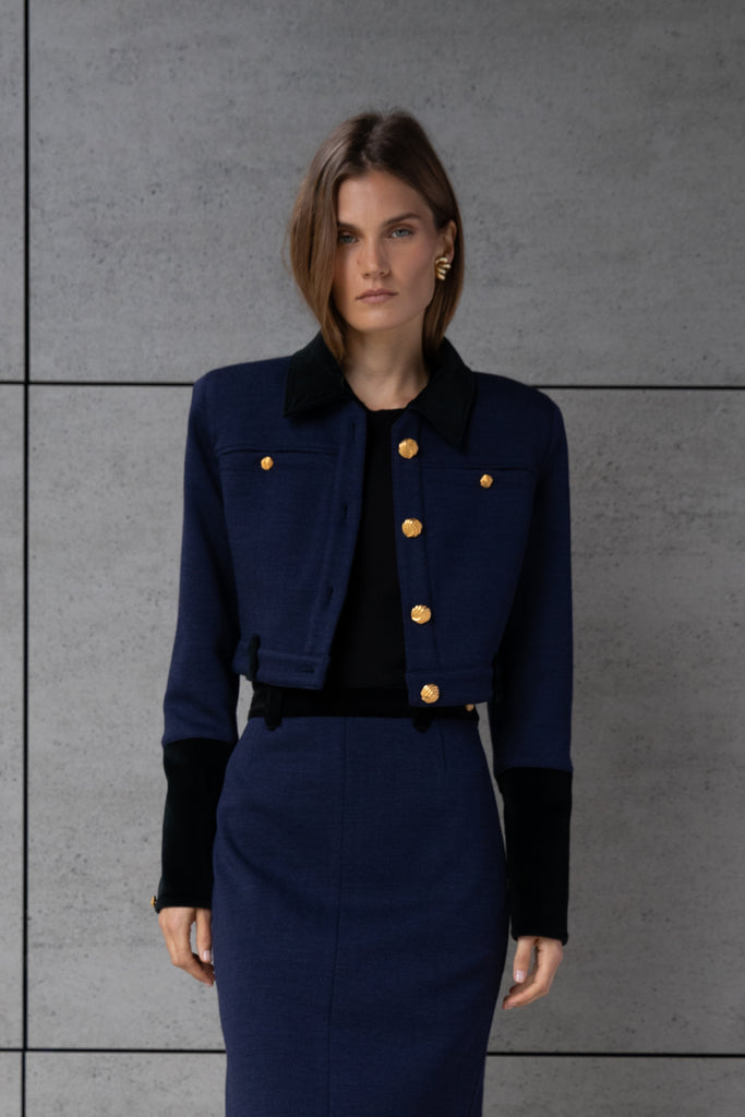 Navy Herringbone Meredith Jacket A fresh take on the classic suit jacket, this cropped style is crafted with fine Italian virgin wool. Detailed contrasting velvet at collar, belt loops, and cuffs. Finished with ROARI's signature gold knot buttons at center front, welt pockets and cuffs. Fully lined.Styled with The Meredith Trouser | The Meredith SkirtAlso available in Black Ostrich *Please reference our return & exchange policy for Sale & Archived items.