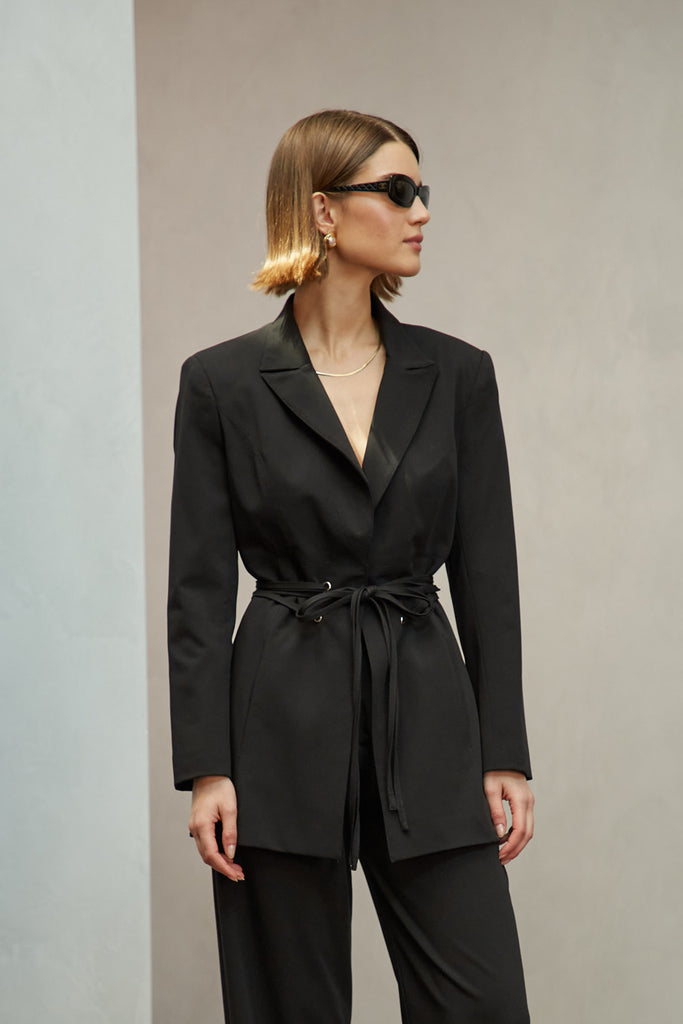 Black Rhodes Blazer This mid-length blazer features a detachable waist tie, allowing you to create a range of looks. The tailored single- breasted style features shoulder pads and front welt pockets. The Kat Trouser compliments the blazer perfectly.Style with The Kat Trouser