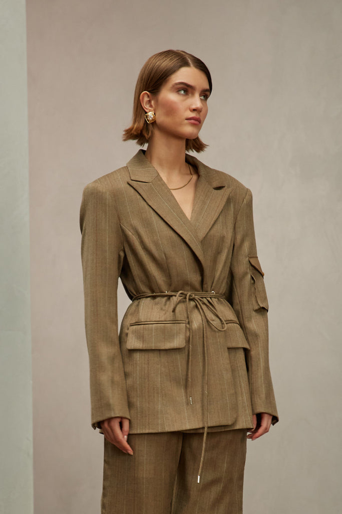 Camel Herringbone Ronnie Blazer Oversized 90's inspired blazer featuring a fixed self-fabric waist tie, cargo pocket detail on left sleeve, two standard flap pockets at hips, and custom selected horn buttons. Ana is 5'9