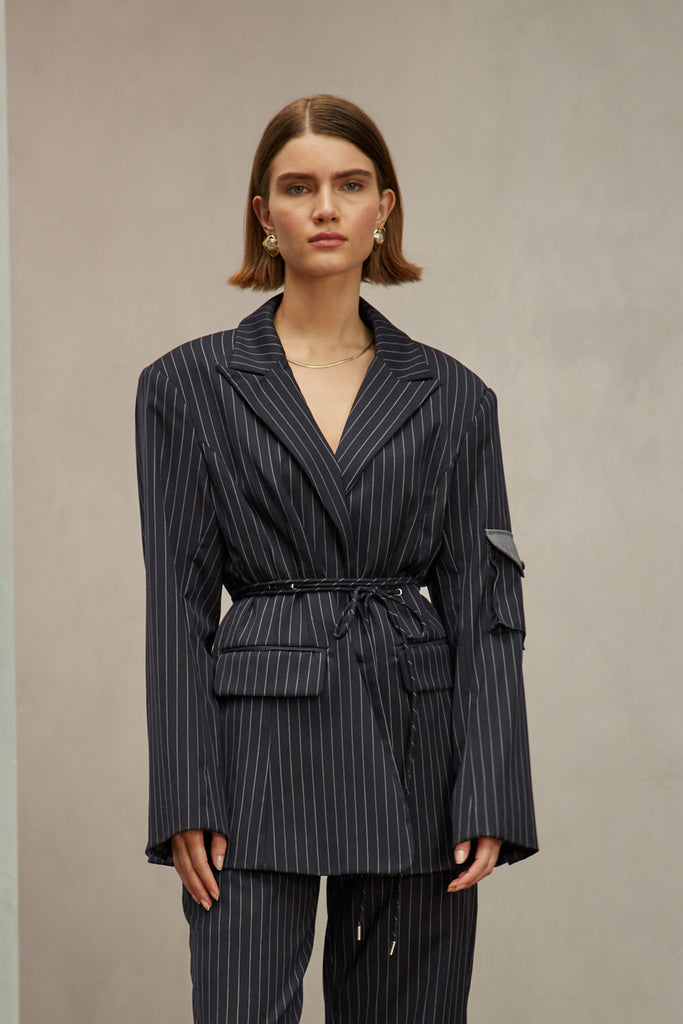 Navy Pinstripe Ronnie Blazer Oversized 90's inspired blazer featuring a fixed self-fabric waist tie, cargo pocket detail on left sleeve, two standard flap pockets at hips, and custom selected horn buttons.Style with The Ronnie Trouser | The Ronnie Corset | The Ronnie Skirt