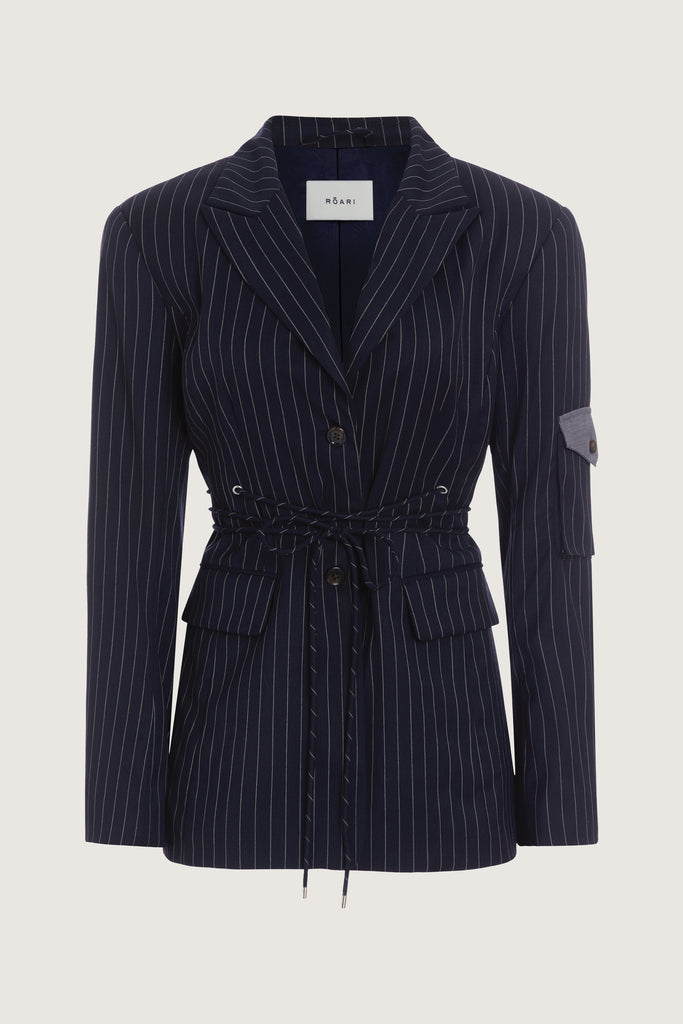 Navy Pinstripe Ronnie Blazer Oversized 90's inspired blazer featuring a fixed self-fabric waist tie, cargo pocket detail on left sleeve, two standard flap pockets at hips, and custom selected horn buttons. Ana is 5'9