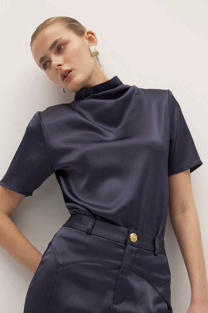 Navy Vivien Top -Cowl neckline with stacked collar-Self-loop and gold knot button at back neck-Removable shoulder pads with interior pockets-French seams for clean finish-1/4” baby hem on sleeves and body-Fluid drape with tailored structure Cara is 5'10